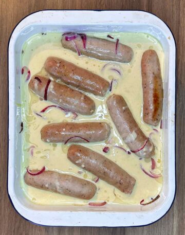 Part cooked sausages and onions surrounded by batter.