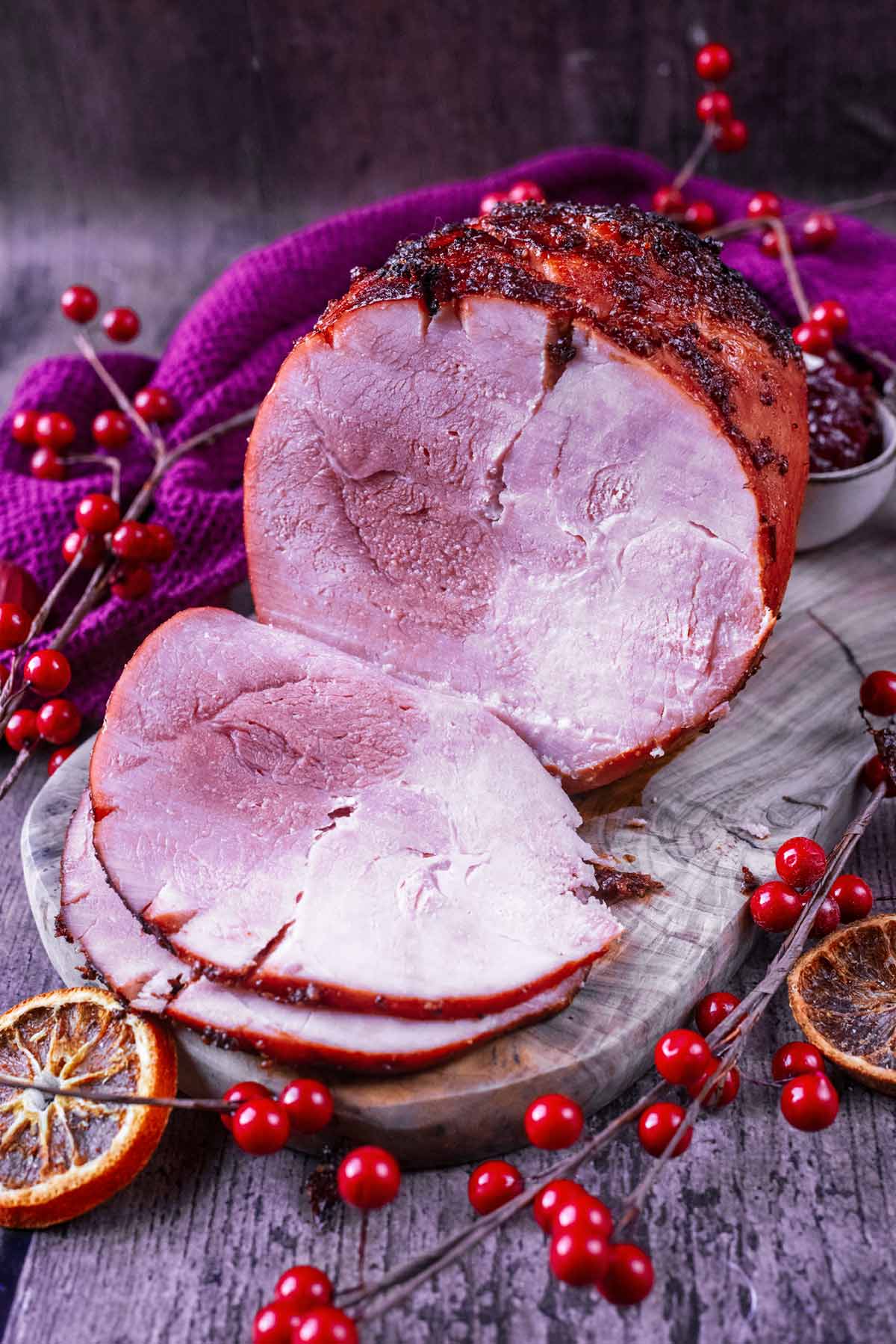 A cooked gammon joint on a wooden board with two slices cut off and folded forward.