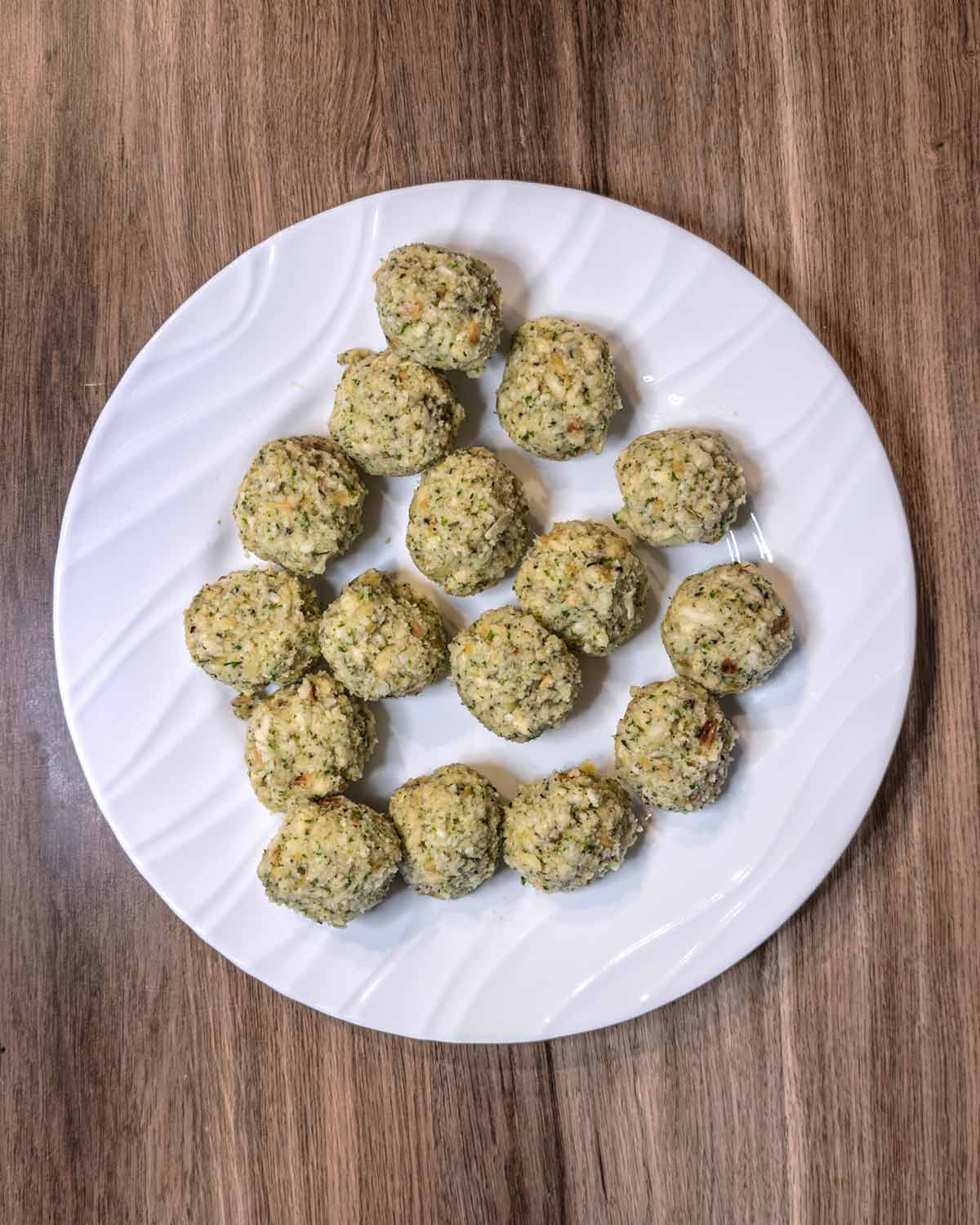 Sixteen uncooked stuffing balls on a plate.