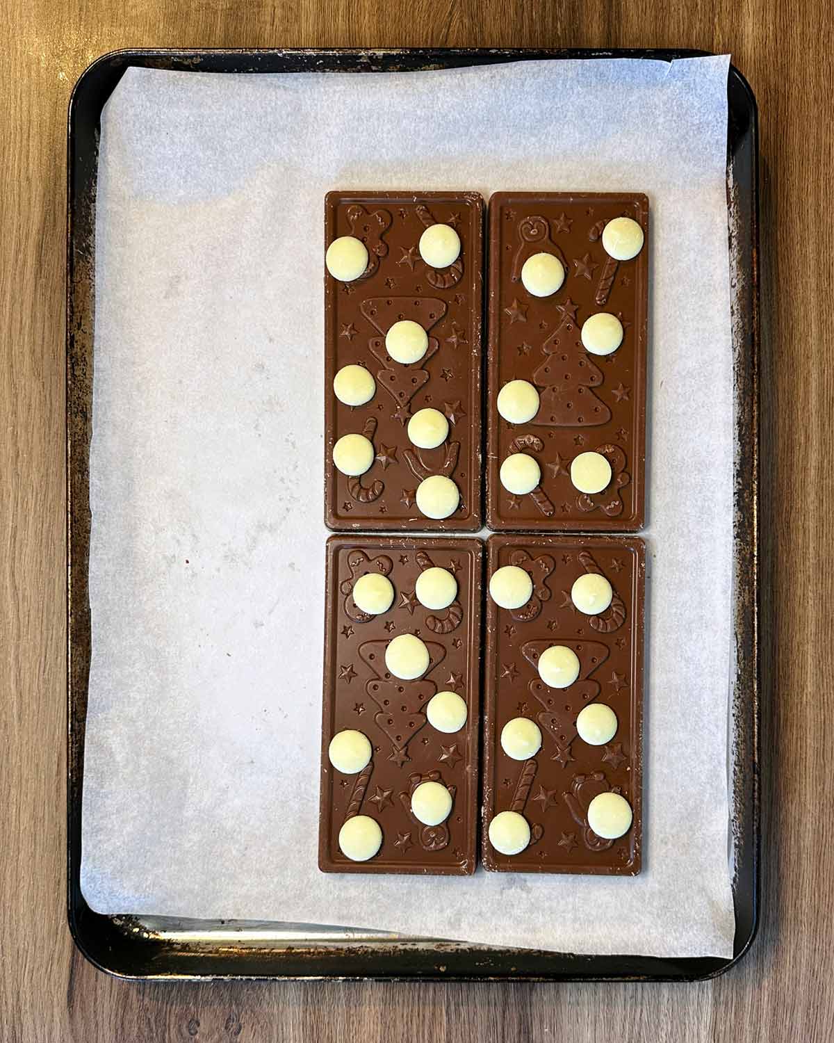 Four bars of chocolate on a lined baking sheet with white chocolate buttons on top of them.