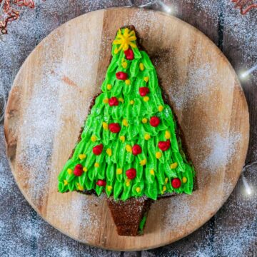 A cake shaped and decorated like a Christmas tree on a round wooden board.