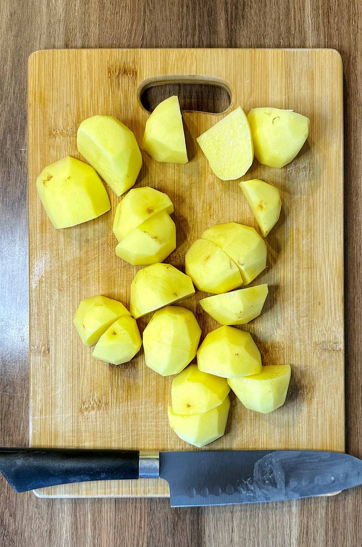 A chopping board with peeled and quartered potatoes on it.
