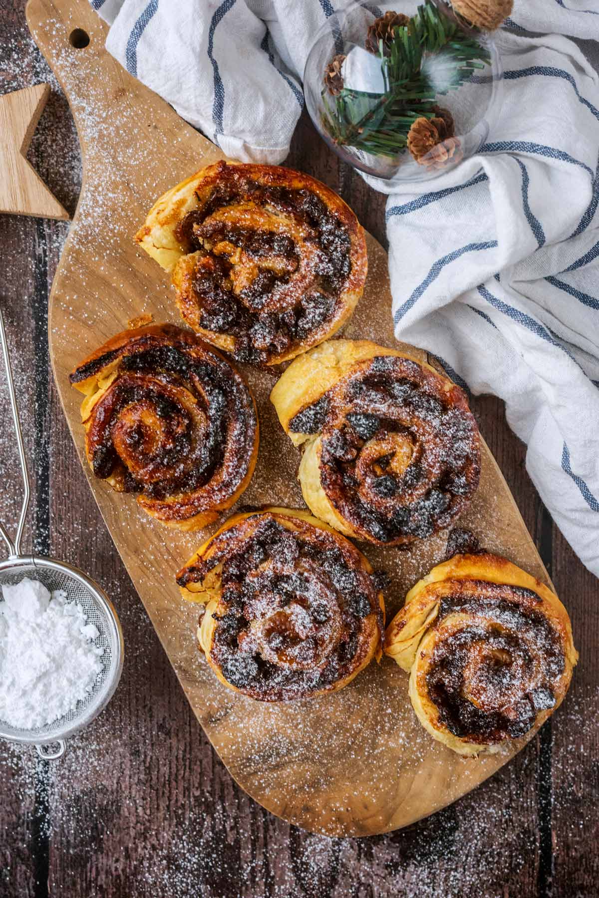 Five mince pie pinwheels on a wooden board next to some icing sugar.