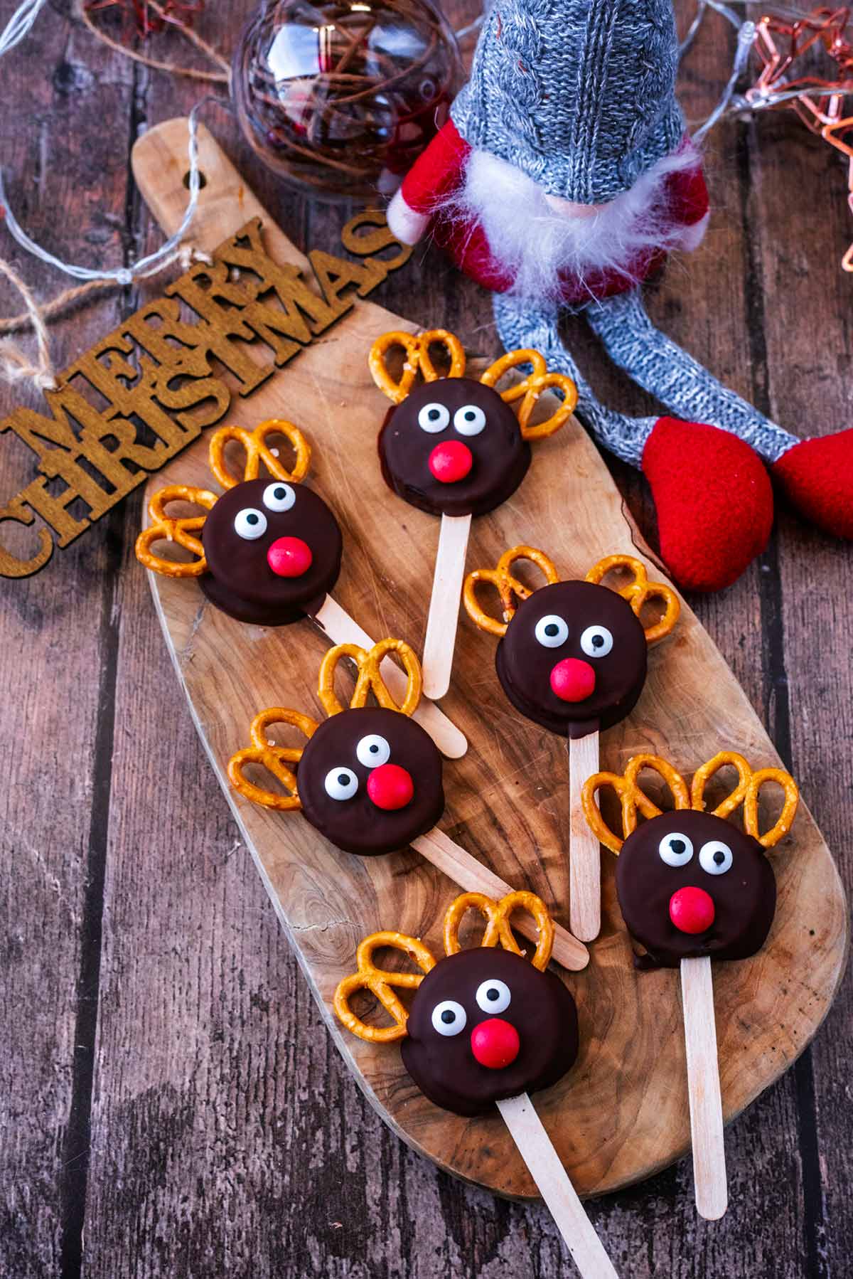 Reindeer oreos on a wooden board next to some Christmas decorations.