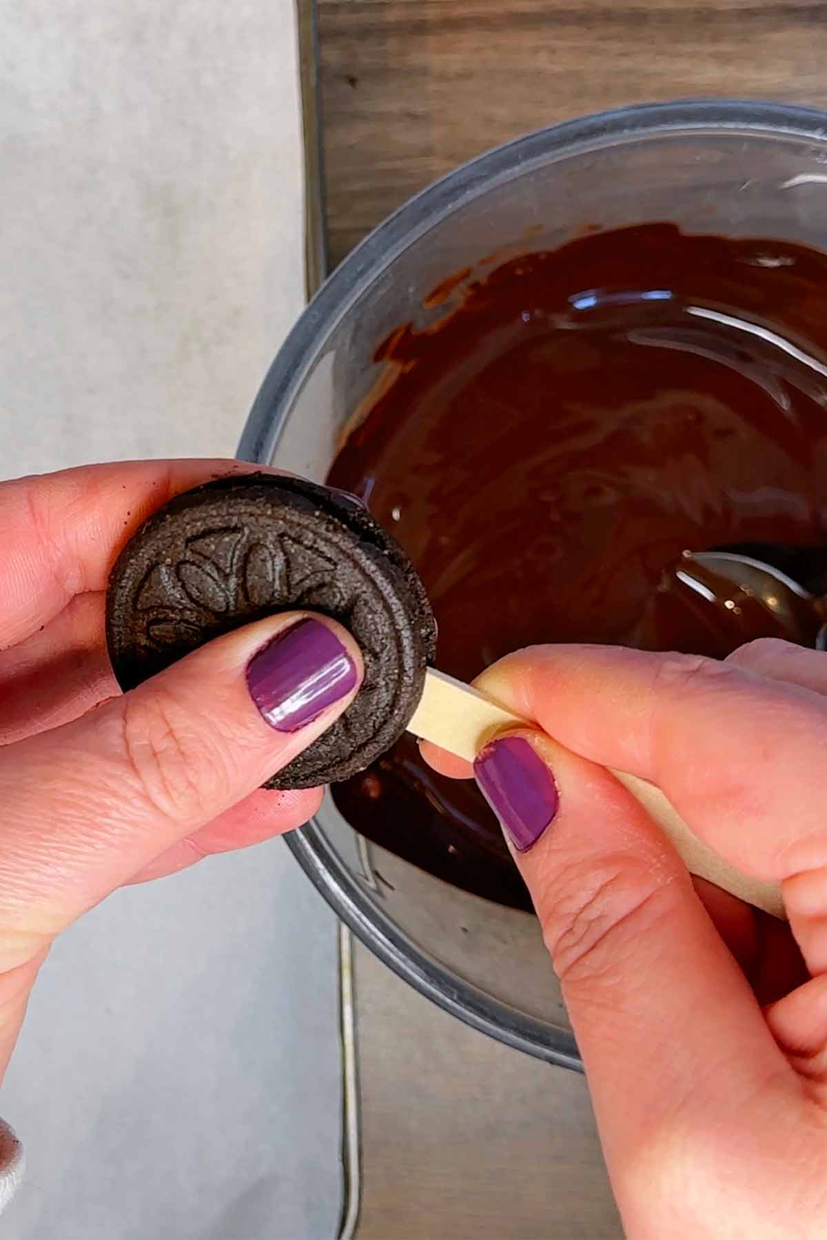 A lollipop stick being pushed into an Oreo cookie.