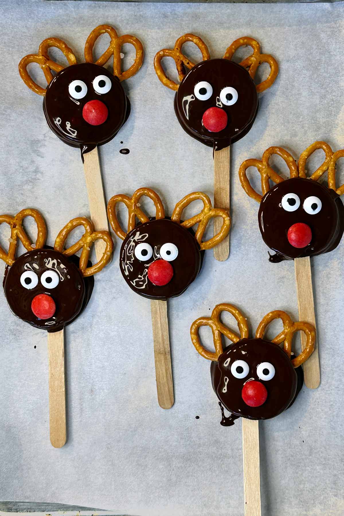 Six coated Oreos on a lined baking tray, decorated like reindeers.