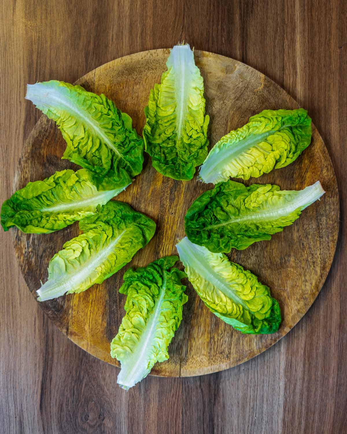 Eight little gem lettuce leaves on a wooden board.