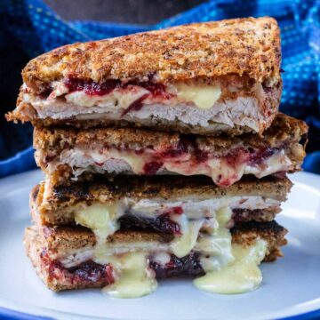 Four turkey grilled cheese sandwiches stacked up with the cheese oozing out.