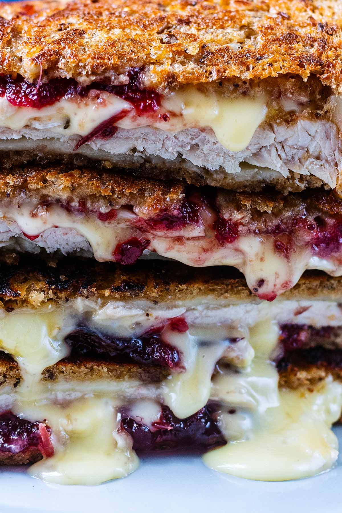 Melted cheese and cranberry sauce oozing out of a toasted sandwich.