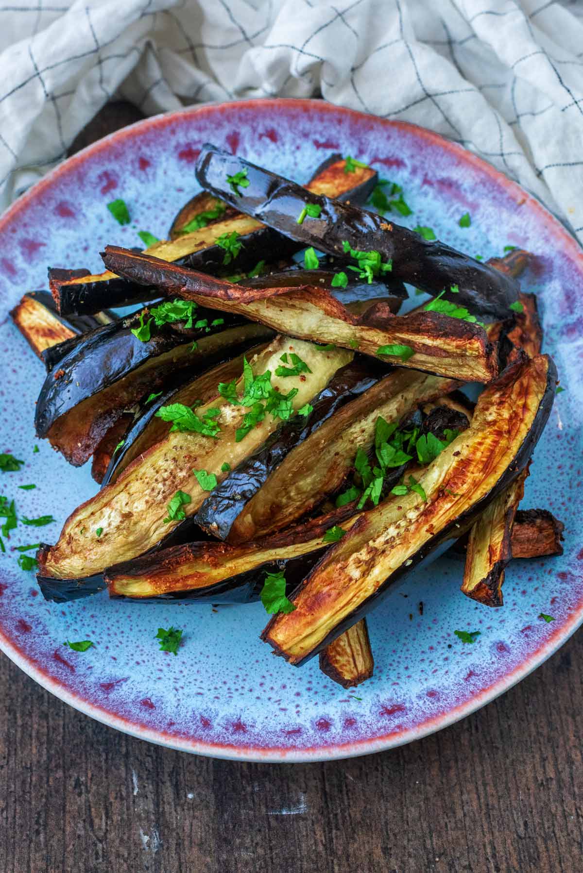 A plate of cooked aubergine in front of a checked towel.