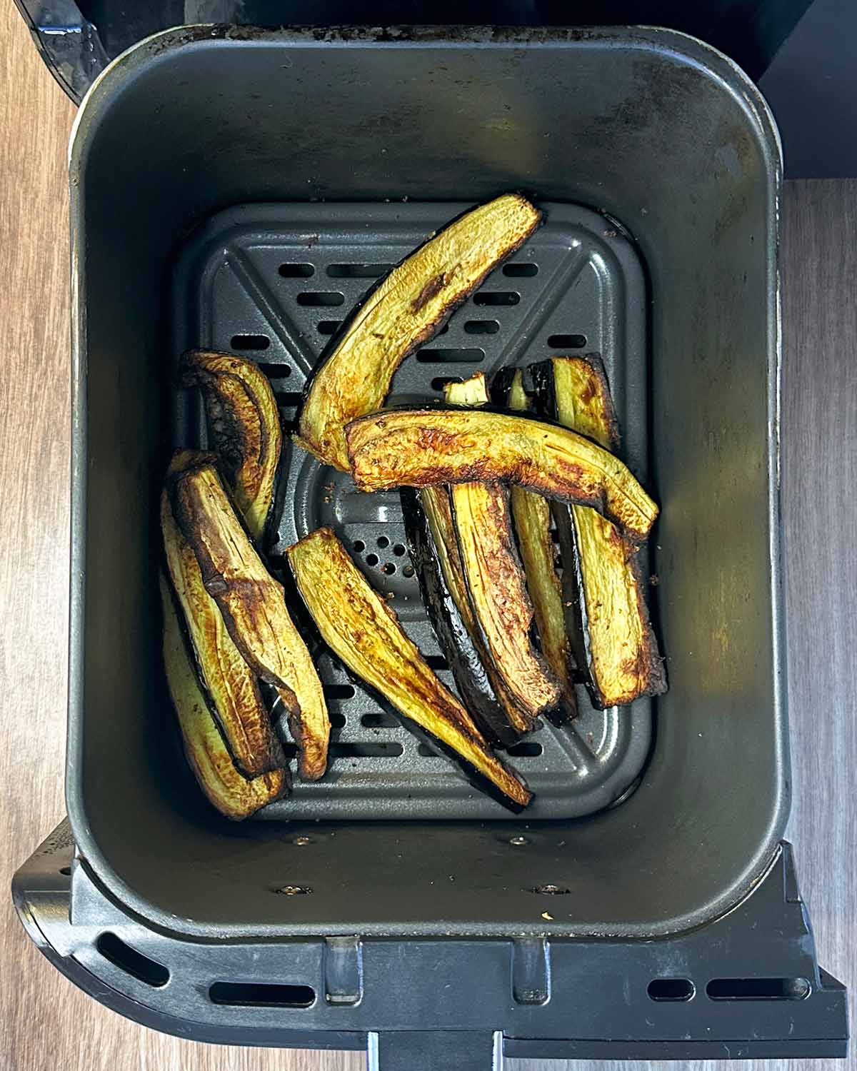 Cooked aubergine strips in an air fryer basket.