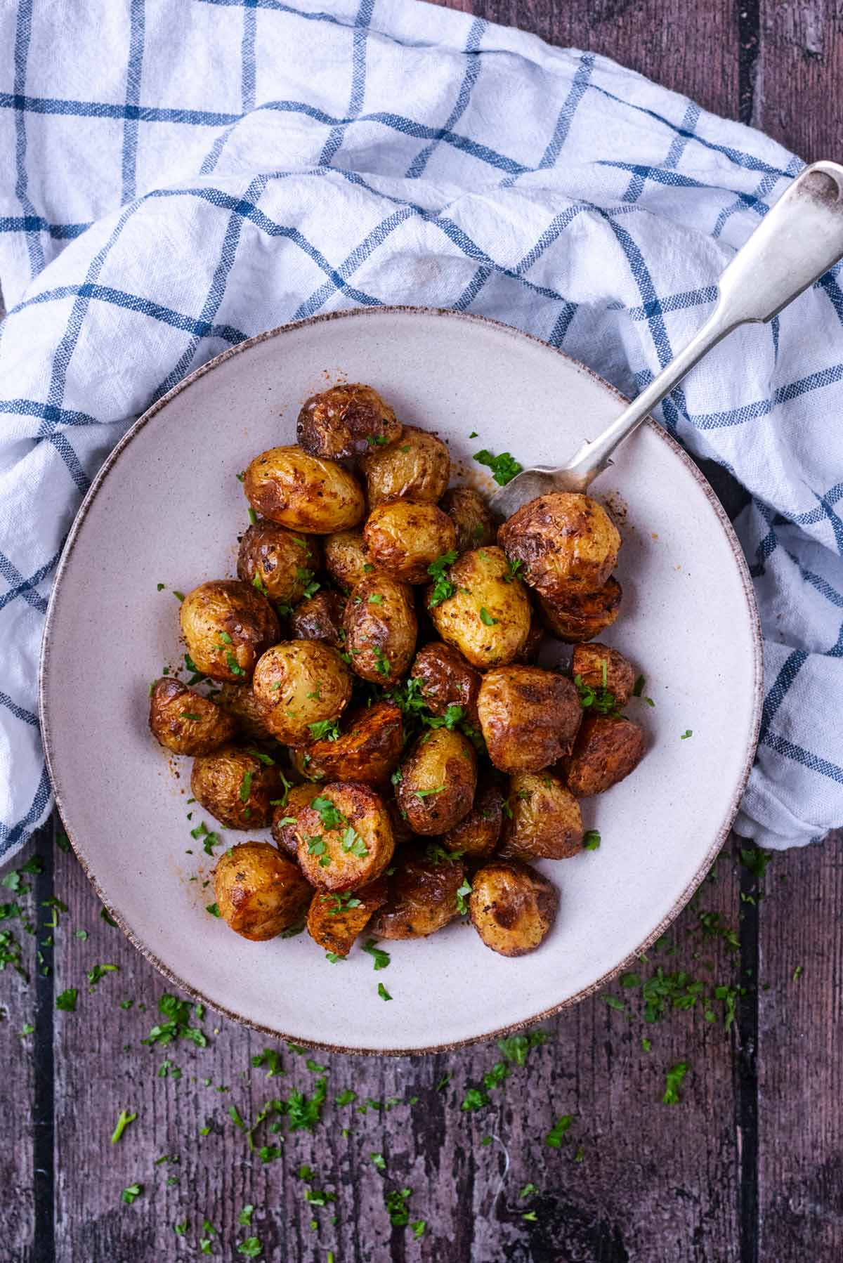 A plate of cooked baby potatoes in front of a checked towel.