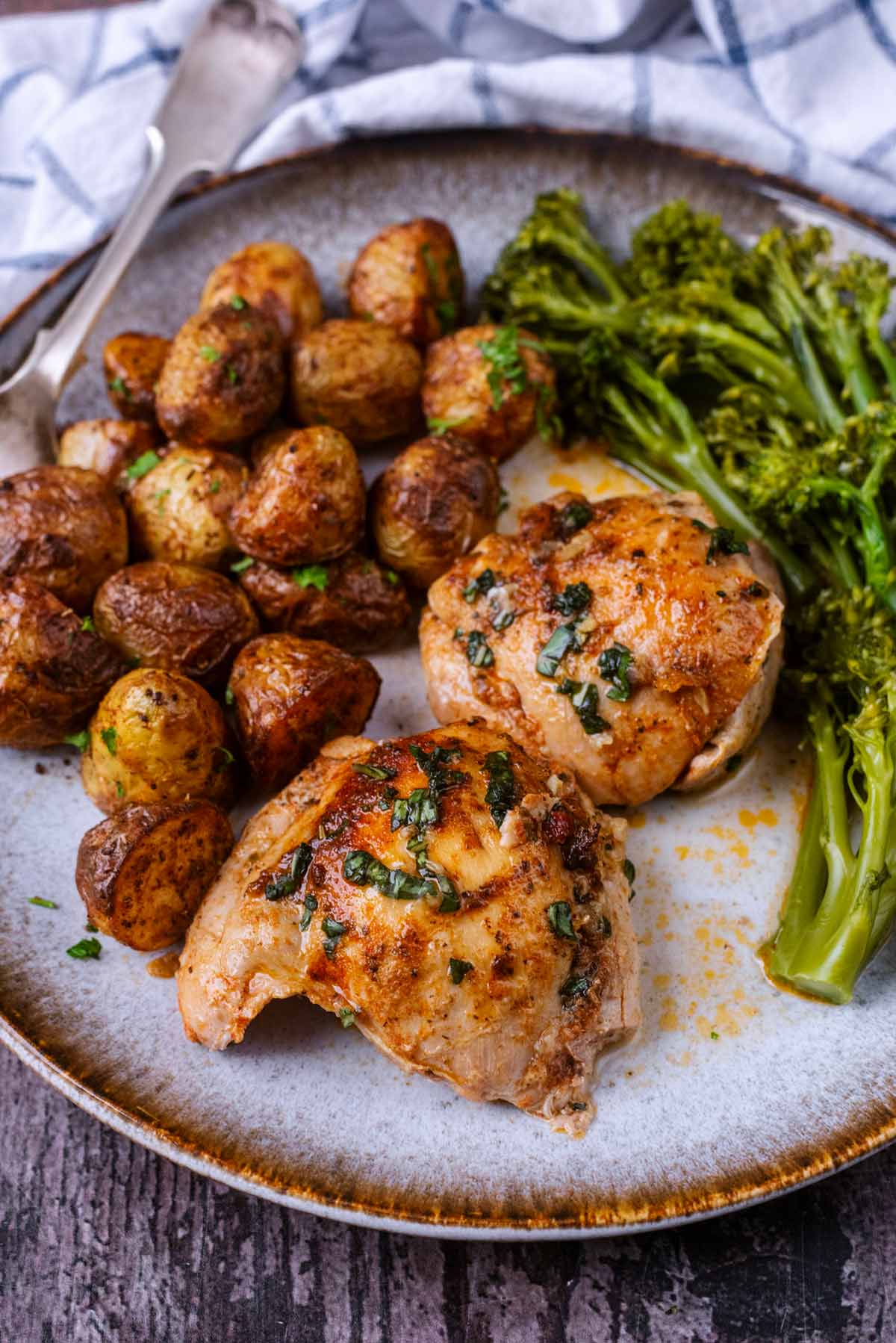 A plate of cooked chicken thighs, new potatoes and tenderstem broccoli.