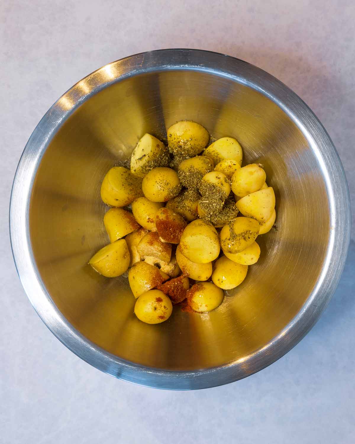 Baby potatoes in a bowl with oil, herbs and seasoning.