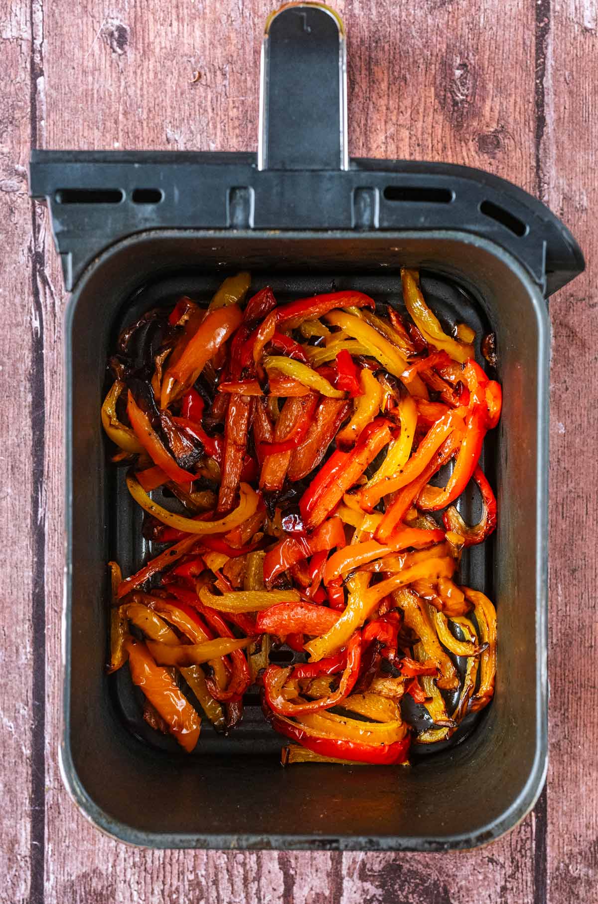An air fryer basket full of cooked red, orange and yellow pepper slices