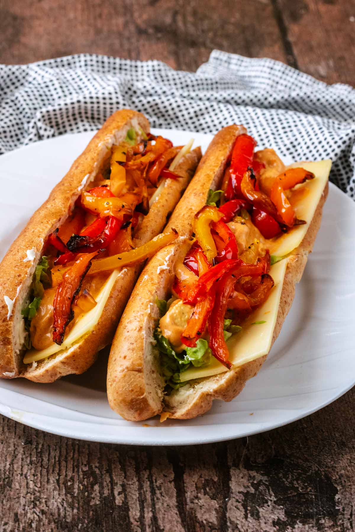 Two baguettes filled with chicken, cheese, salad and topped with cooked pepper strips.