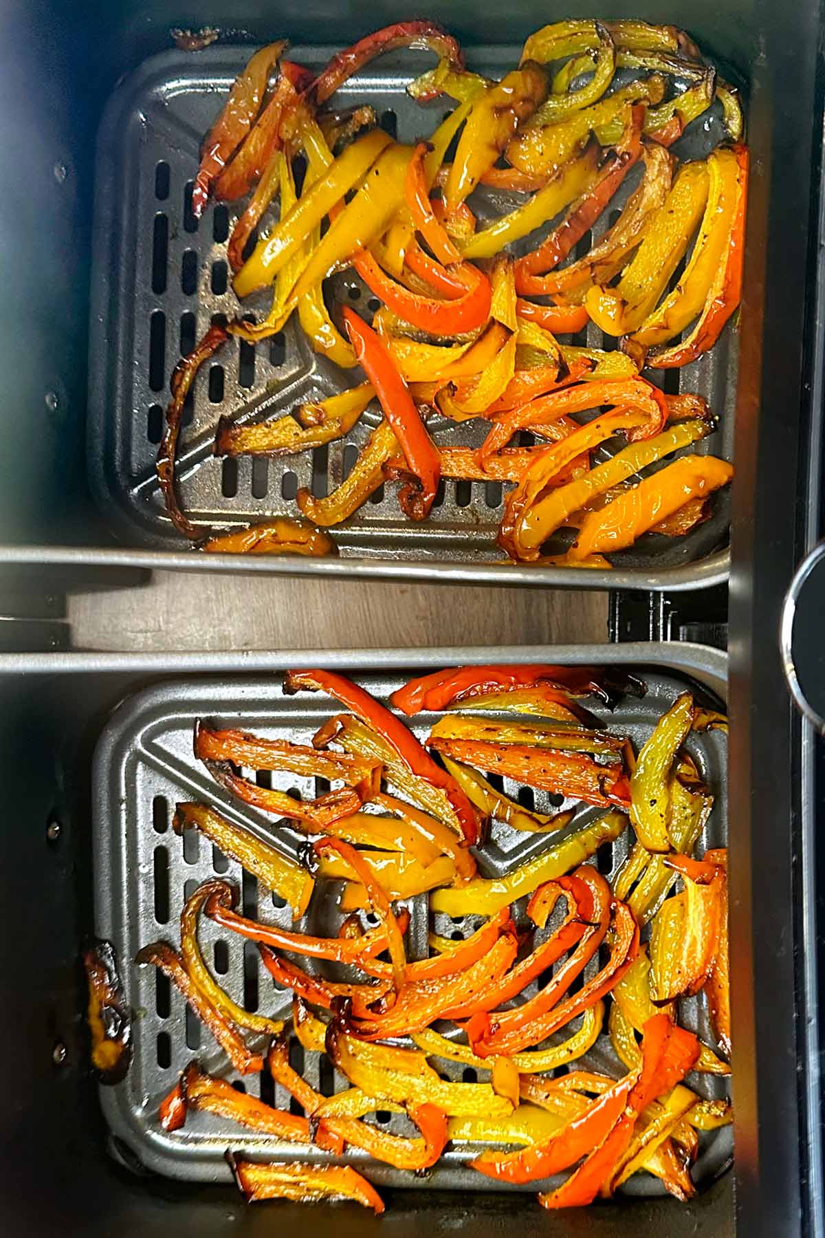 Cooked strips of bell pepper in two air fryer baskets.