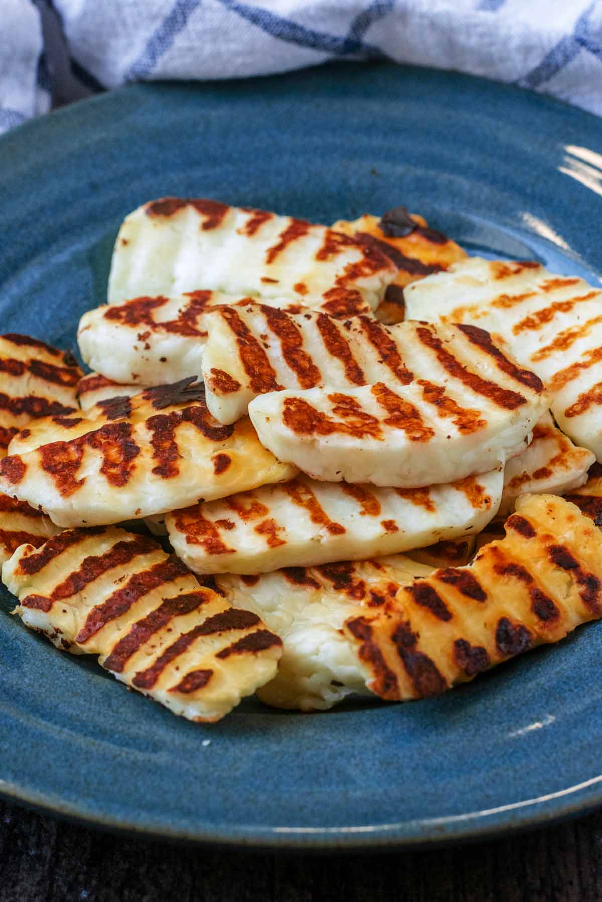 Cooked halloumi slices on a blue plate in front of a checked towel.
