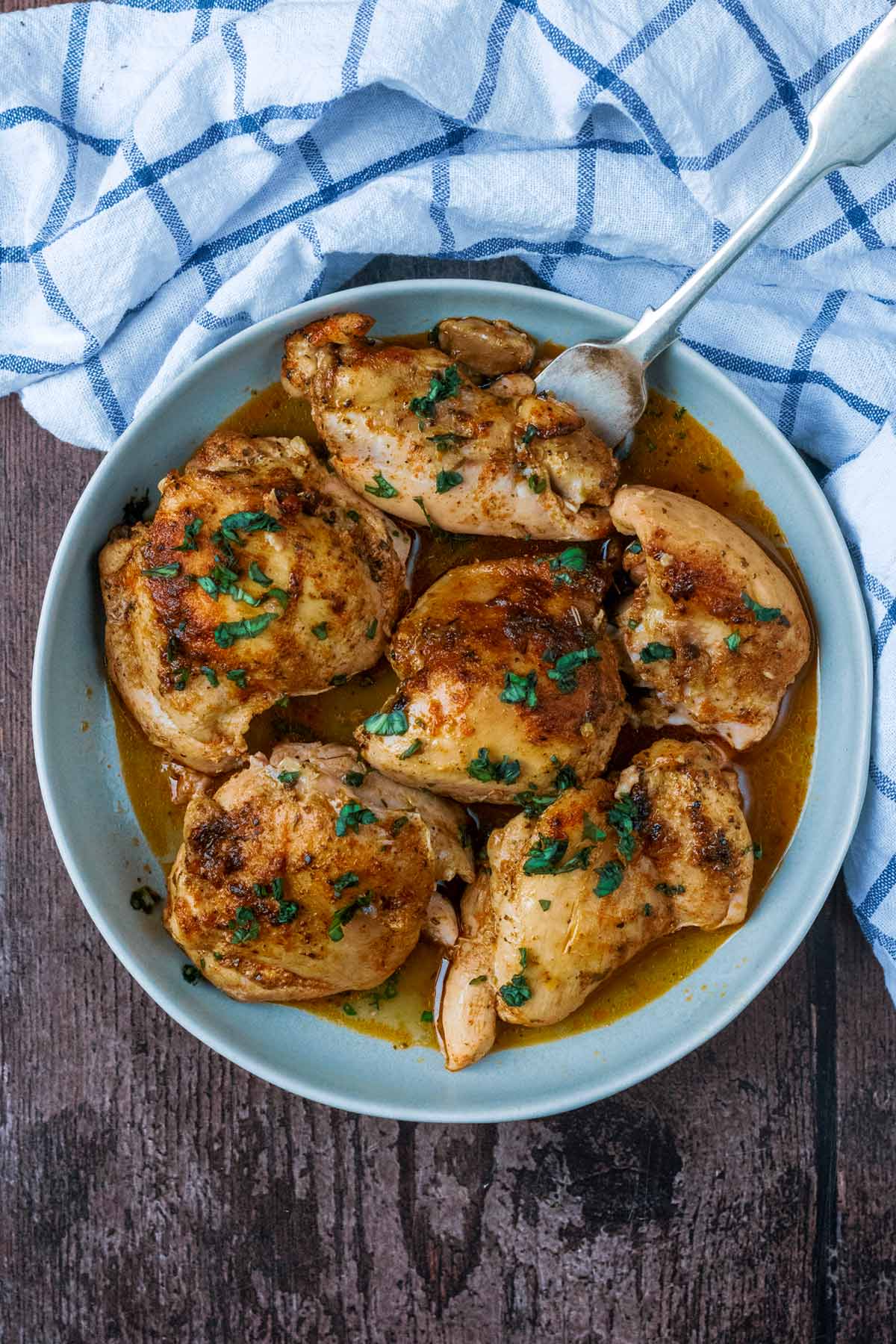 Cooked chicken thighs on a blue plate with a fork.