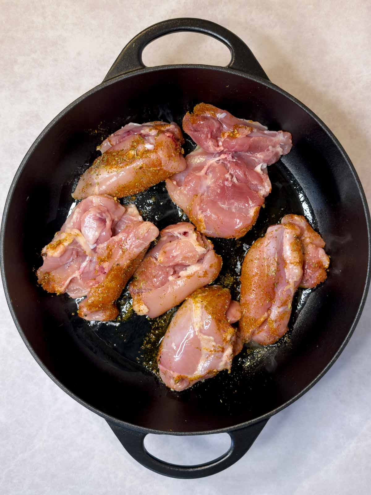 Chicken thighs cooking in a large black pan.