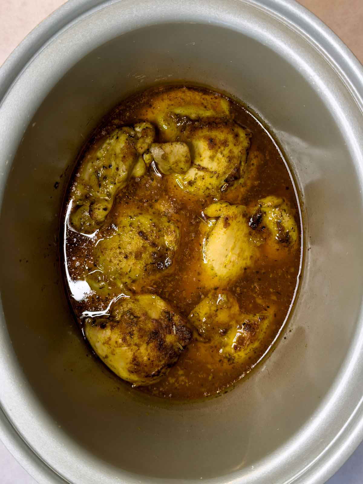 Cooked chicken thighs in stock in a slow cooker.