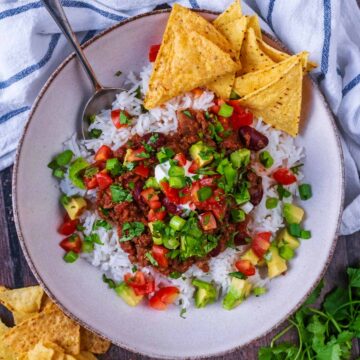 Slow cooker chilli con carne in a bowl with tortilla chips and rice.