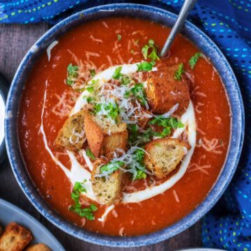 A bowl of slow cooker tomato soup topped with cream, croutons and herbs.