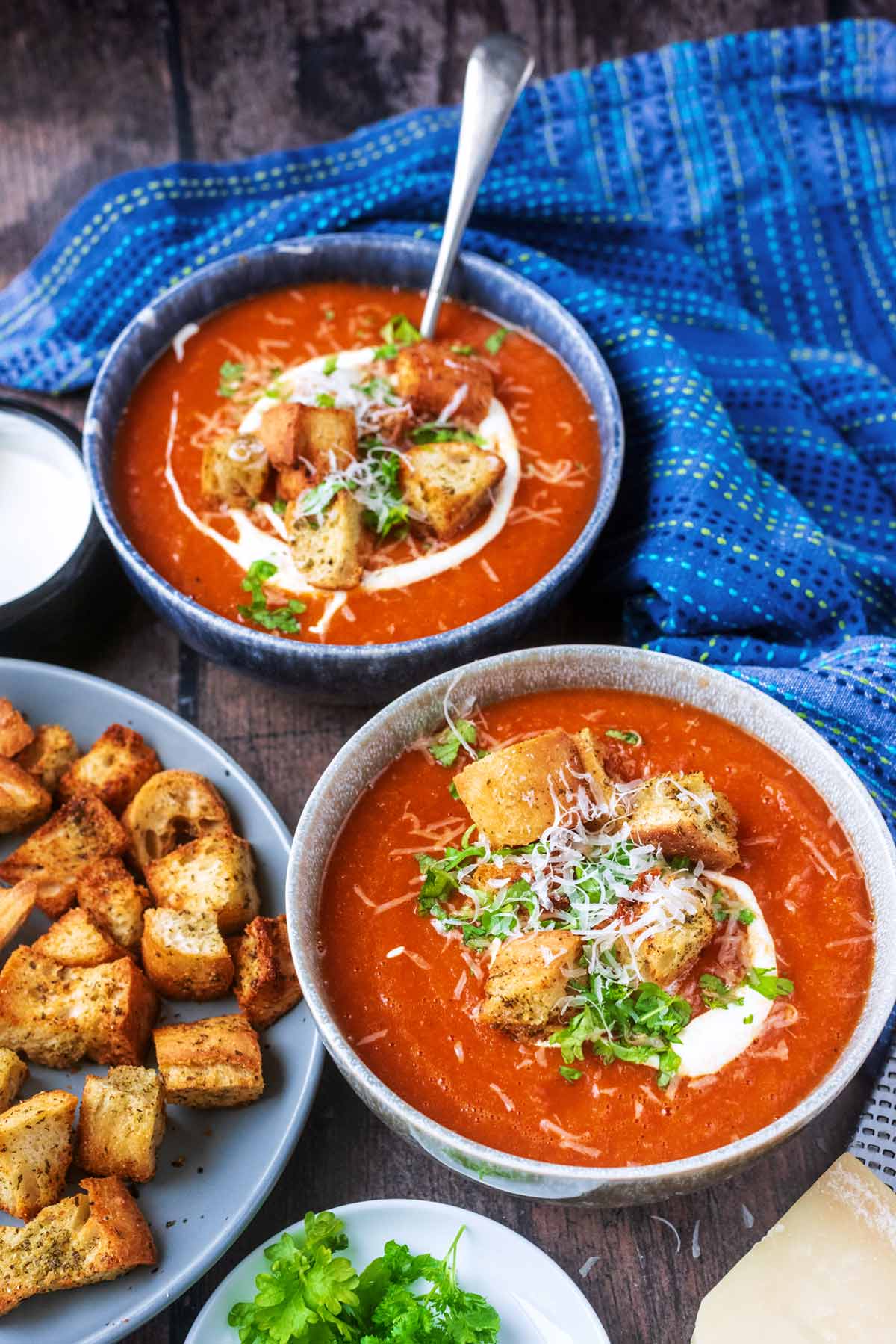 Two bowls of tomato soup in front of a blue towel.