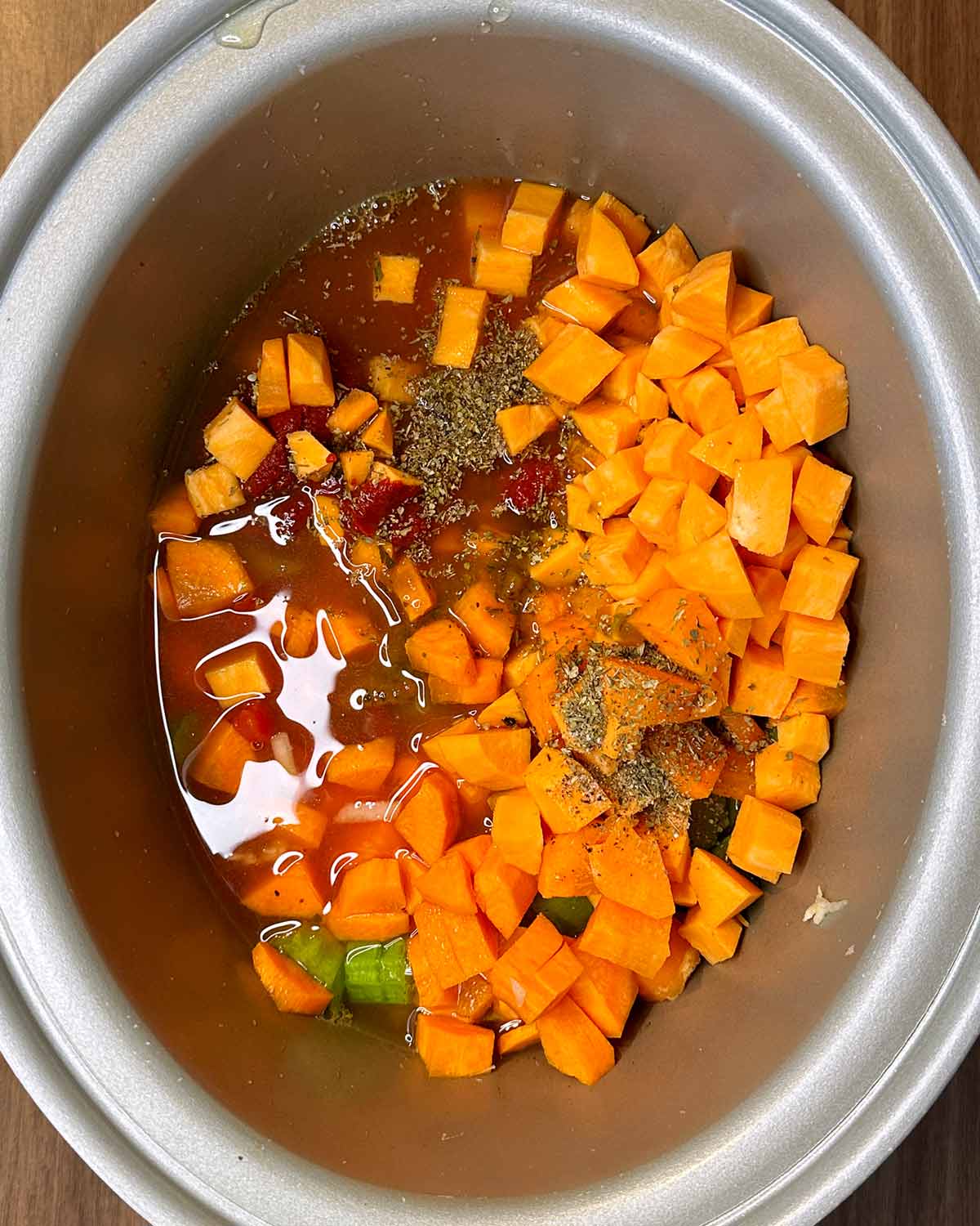Chopped vegetables, tomatoes, stock and seasoning in a slow cooker bowl.