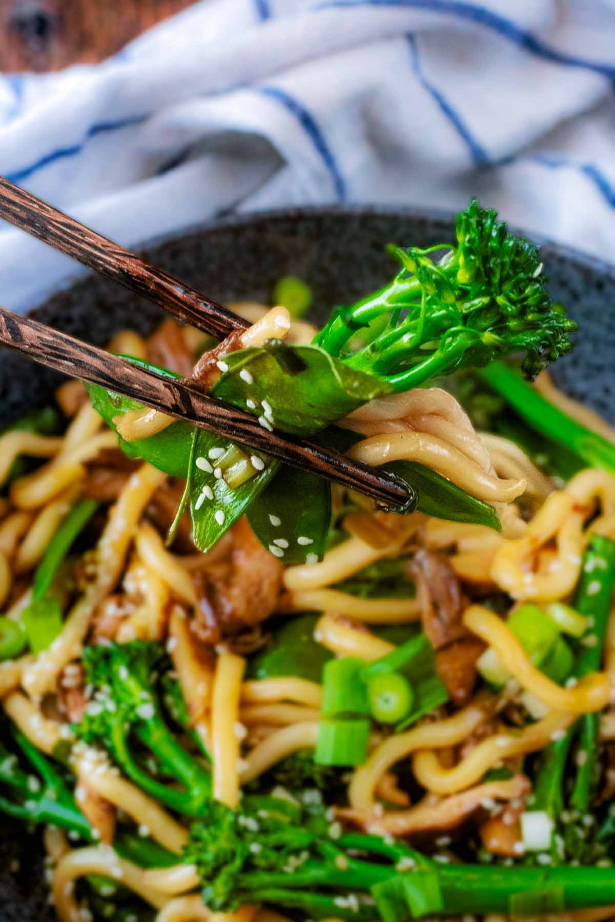 A pair of chopsticks picking up some broccoli and noodles from a bowl.