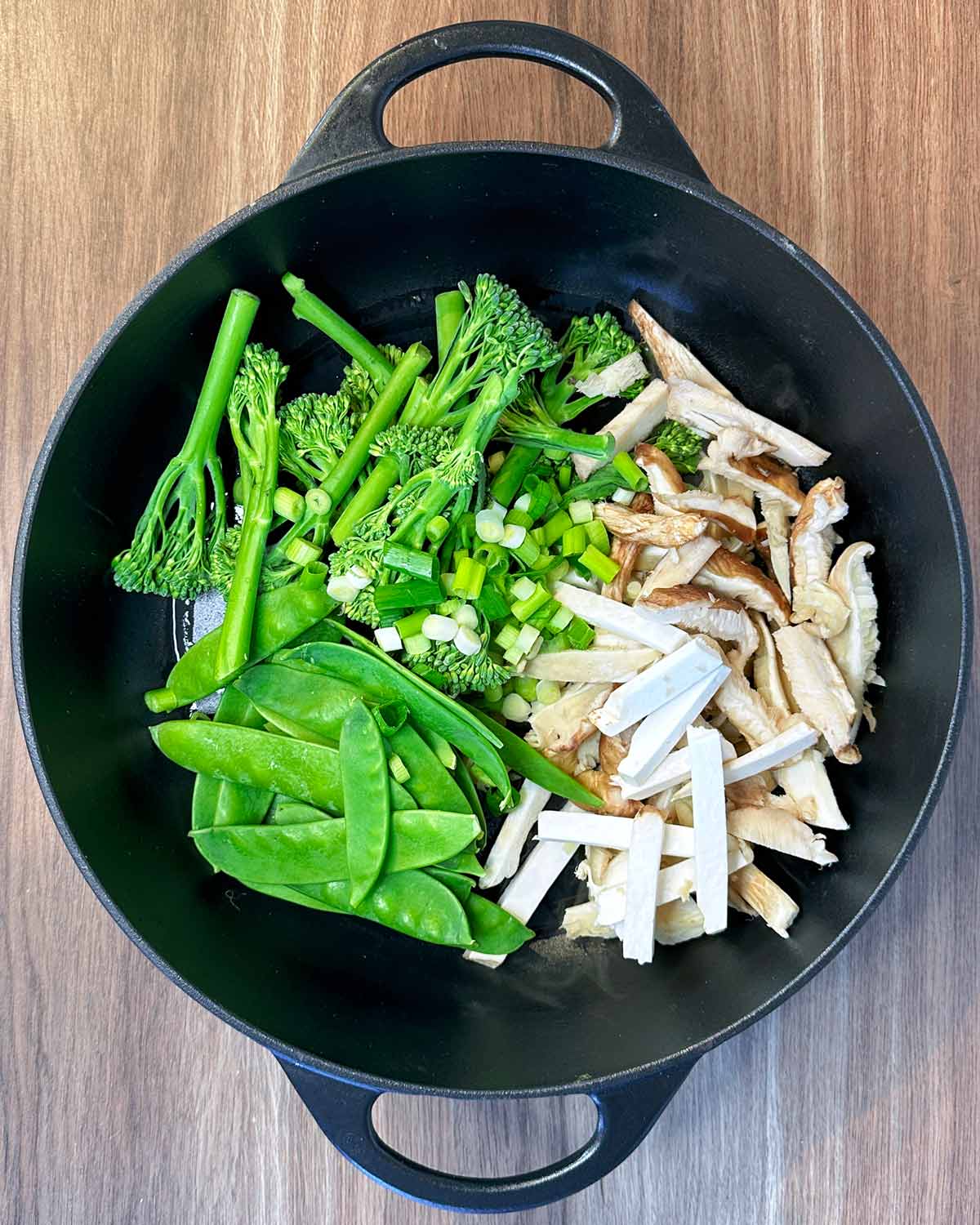 Mushrooms, broccoli, spring onions and mangetout frying in a pan.