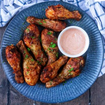 Eight air fryer chicken drumsticks on a plate with a pot of dip.