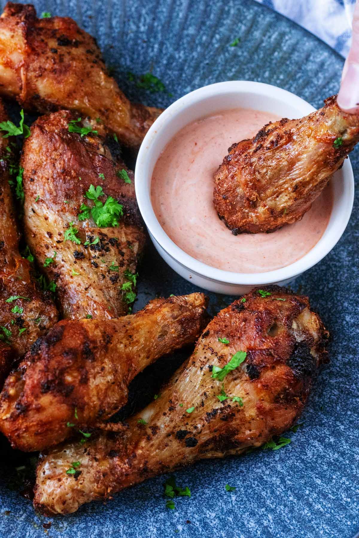 A cooked chicken drumstick being dipped in a small pot of sauce.