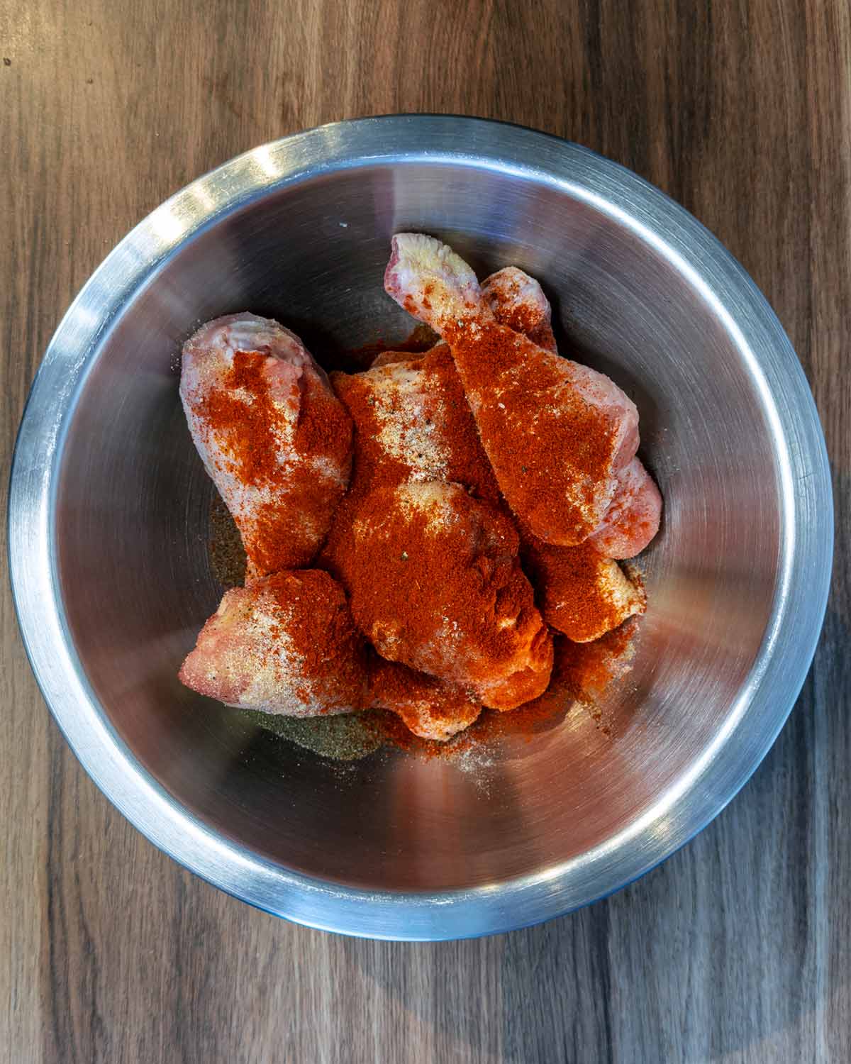 Raw chicken drumsticks in a bowl with oil and seasoning.