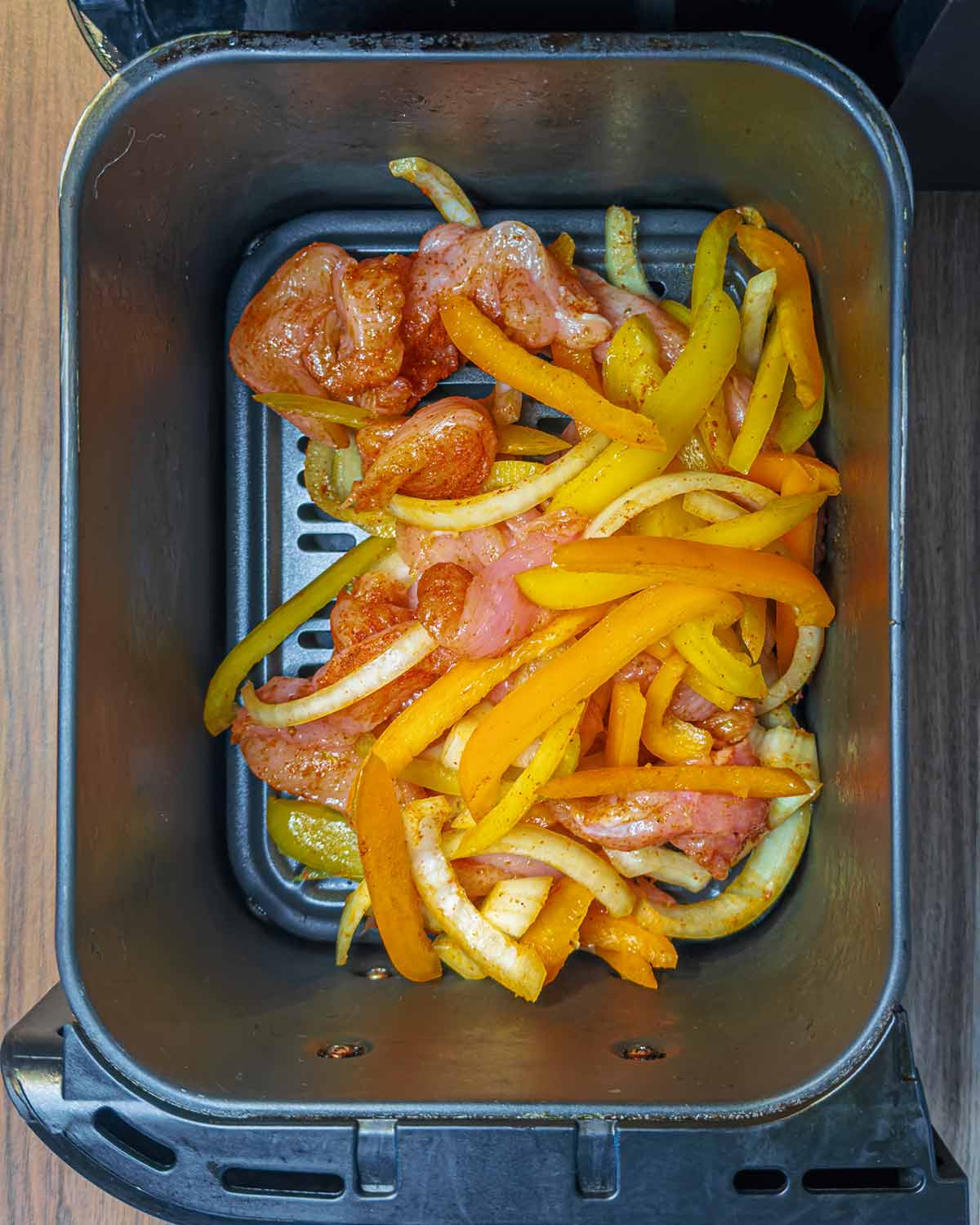 Coated chicken, peppers and onions in an air fryer.