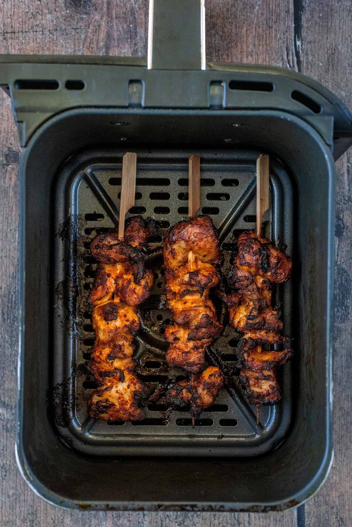 An air fryer basket with three cooked chicken kebabs in it.