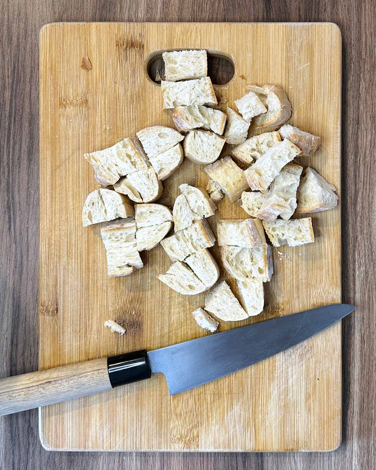 Bread chopped into cubes on a wooden chopping board.