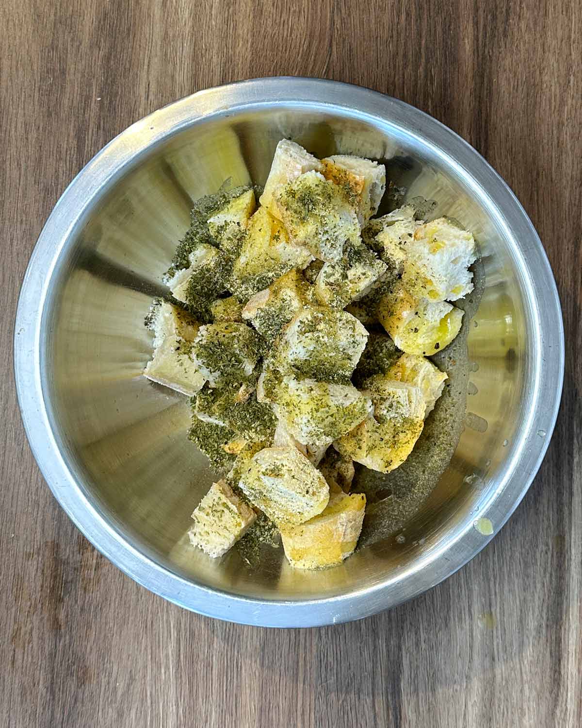 Cubes of bread in a bowl with melted butter and seasoning.