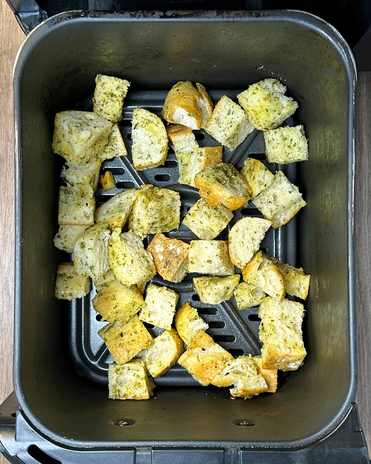Coated chunks of bread in an air fryer basket.