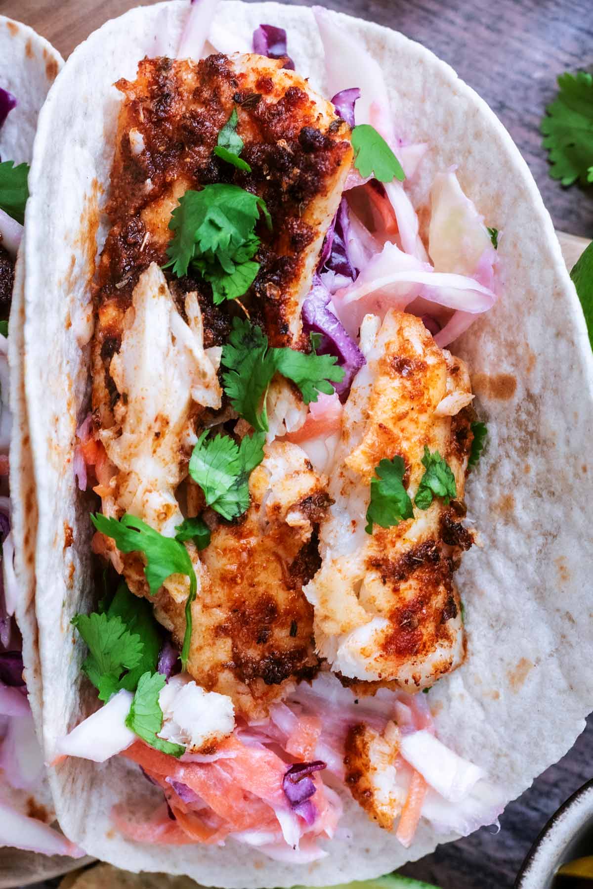 Cooked seasoned cod in a soft taco shell with slaw and coriander.