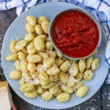 A plate of air fryer gnocchi with a bowl of marinara.