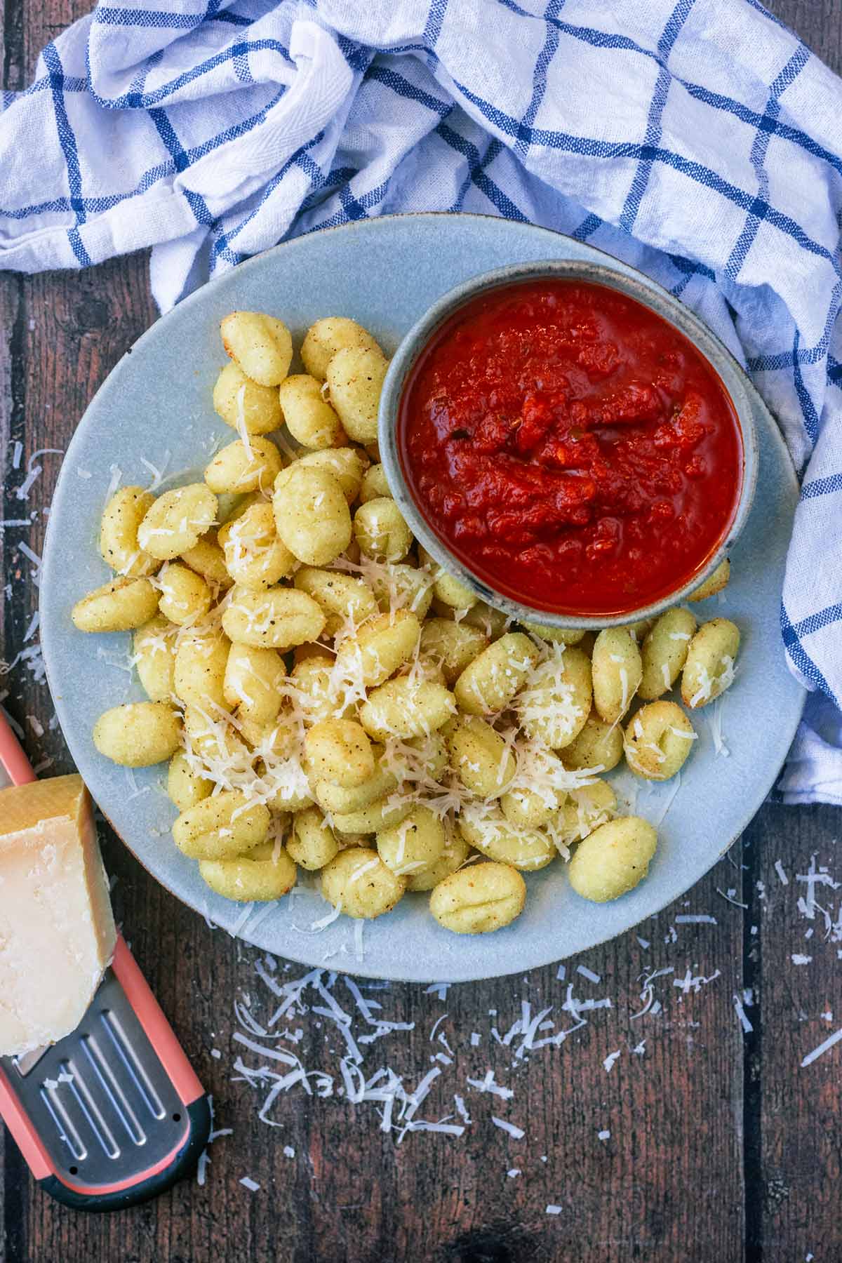 A plate of cooked gnocchi next to a bowl of marinara and a block of Parmesan.