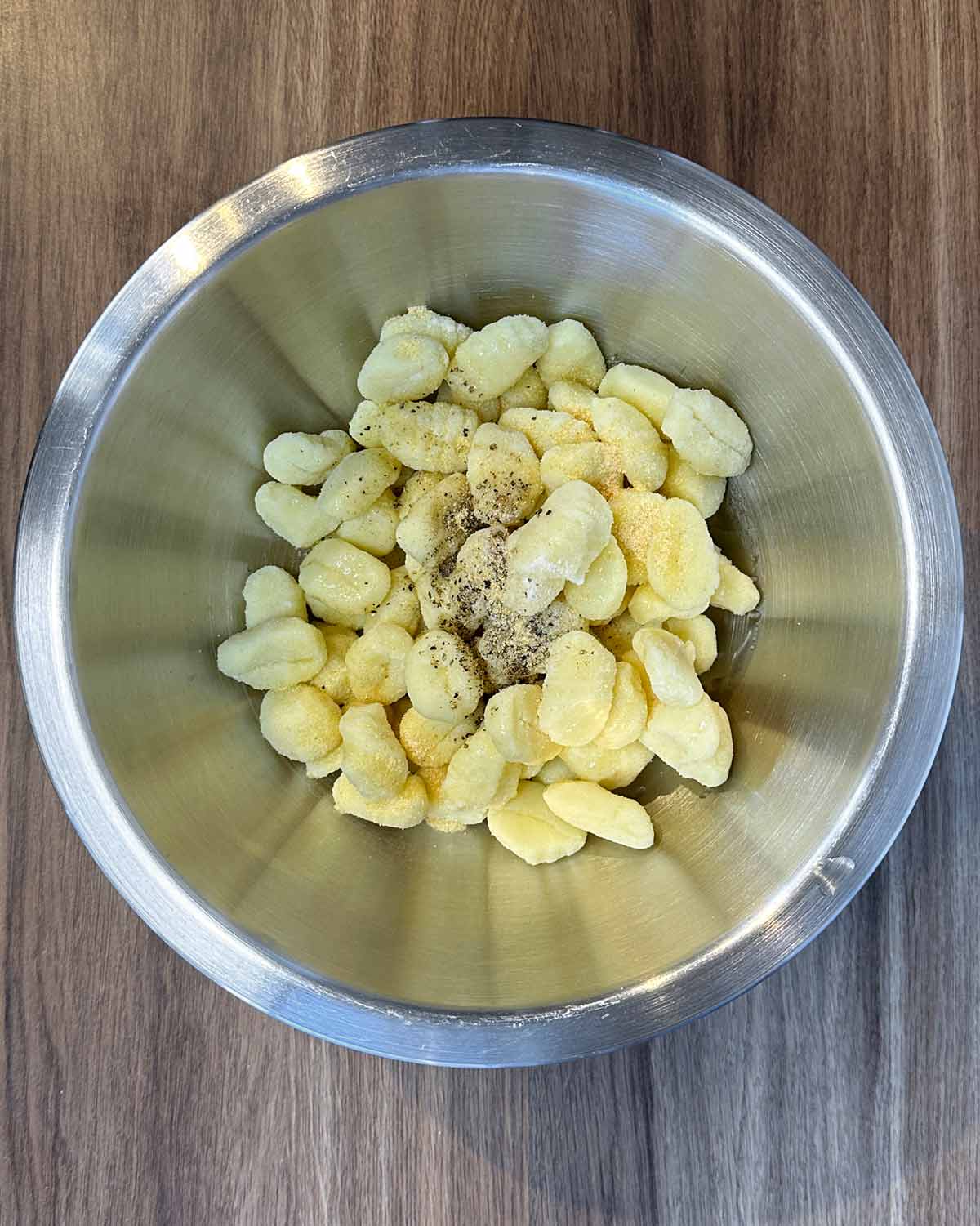 A bowl of uncooked gnocchi with oil and seasoning.