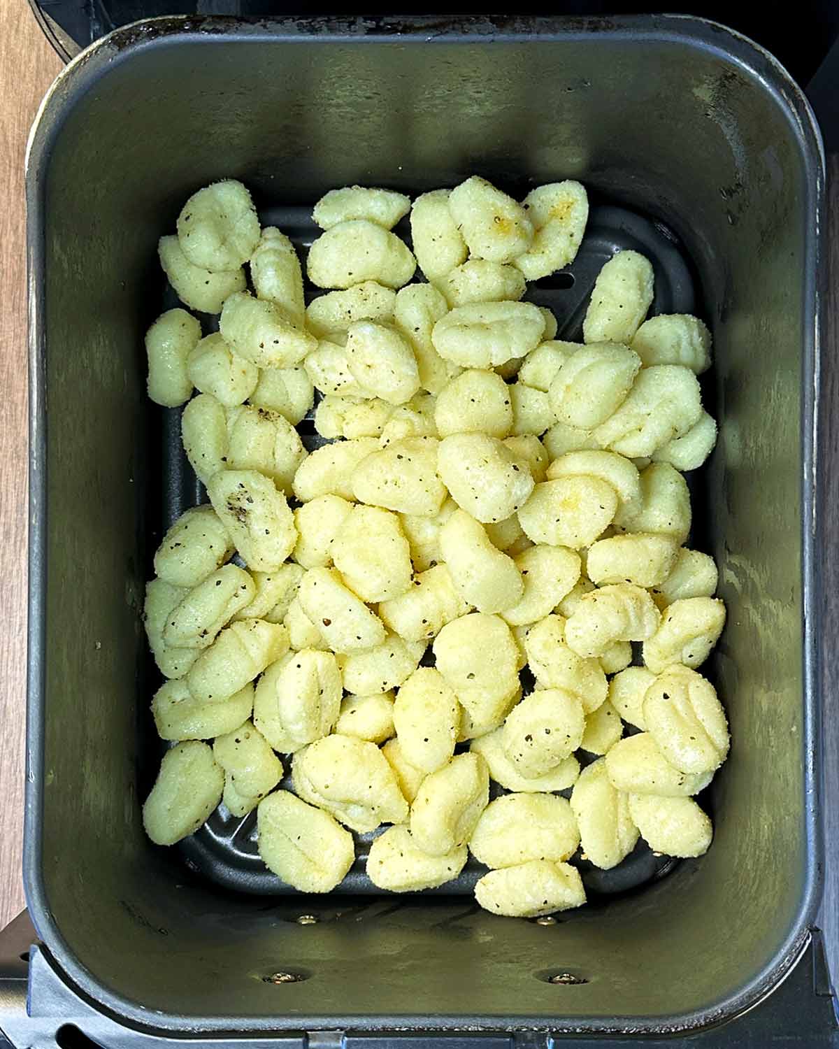Coated gnocchi in an air fryer basket.