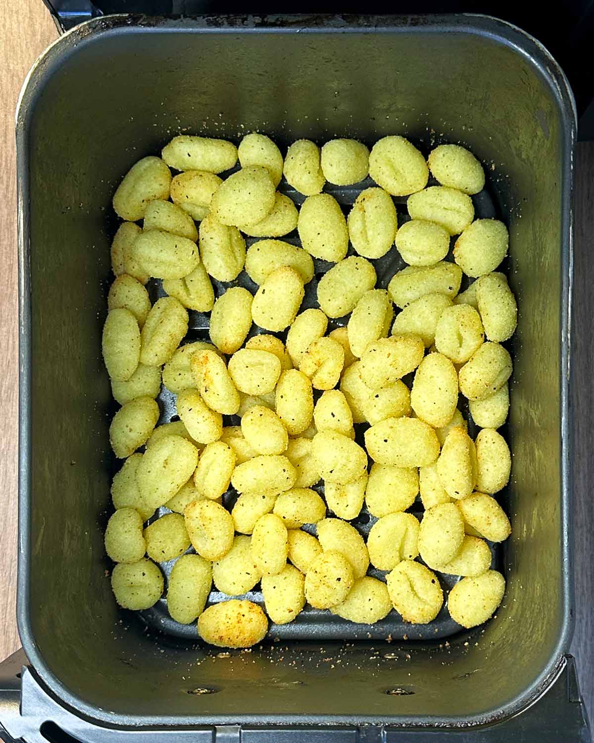 Cooked gnocchi in an air fryer basket.