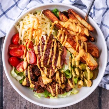 Burger in a bowl with salad, chips and sauce.