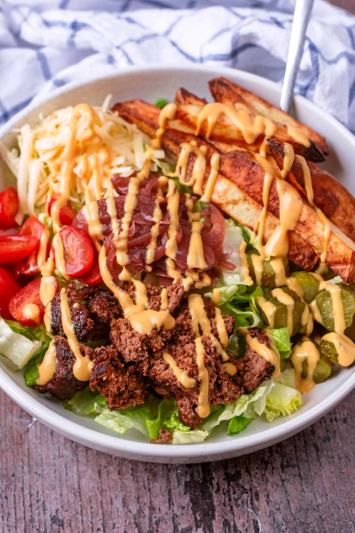 A fork in a bowl of burger and salad ,all topped with drizzles of burger sauce.