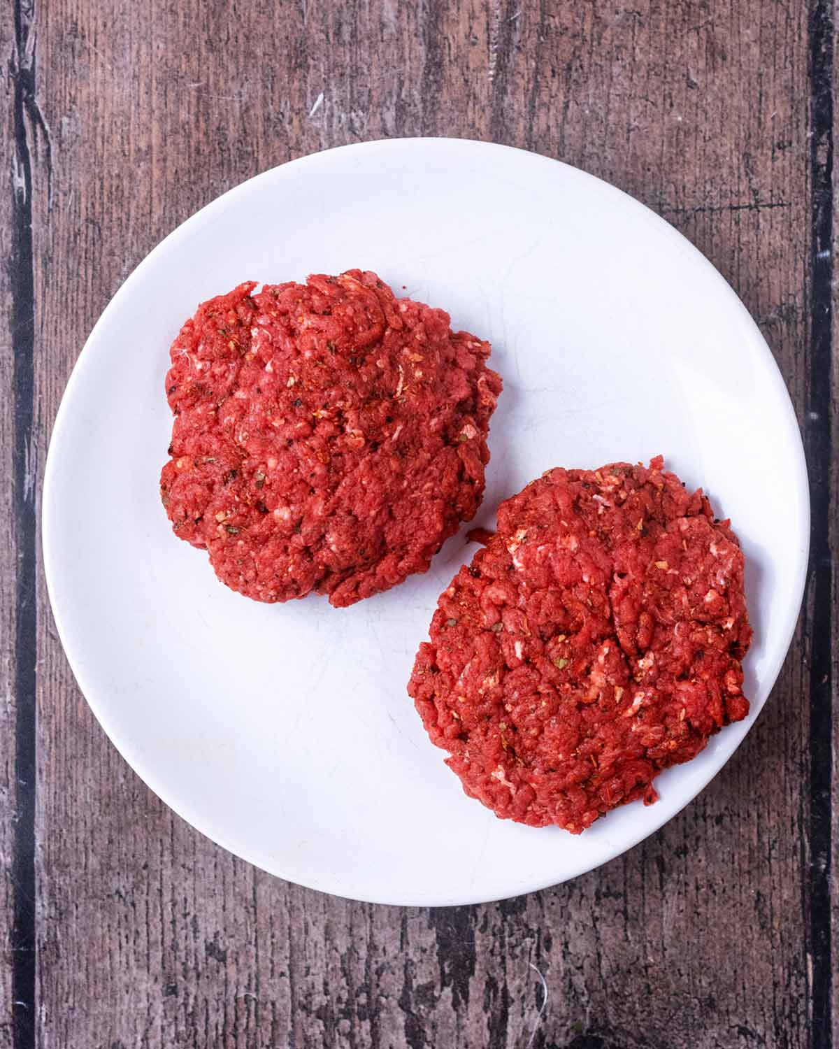 Two uncooked burger patties on a white plate.