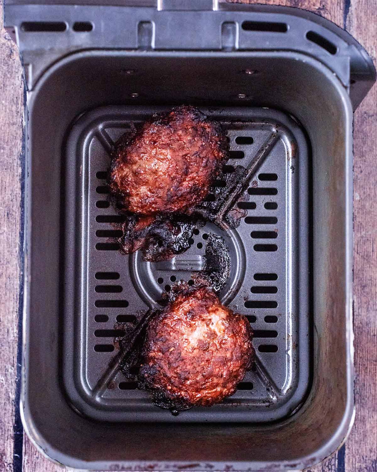 Two cooked burgers in an air fryer.