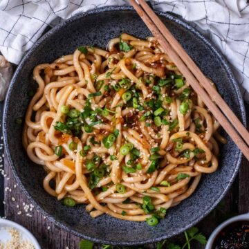 Chilli oil noodles in a grey bowl with a pair of chopsticks across the bowl.